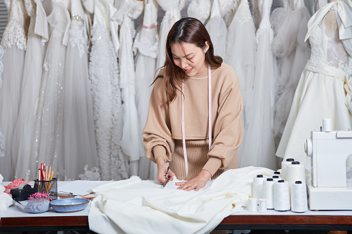 A wedding dress rental shop owner standing cut the fabric on her desk. Woman dressmaker in her bridal boutique. Small business entrepreneur concept.
