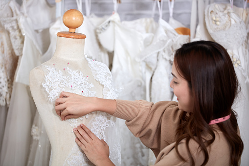 A wedding dress rental shop owner standing working with a mannequin and equipment. Women dressmaker in her bridal boutique. Small business and marriage concept.