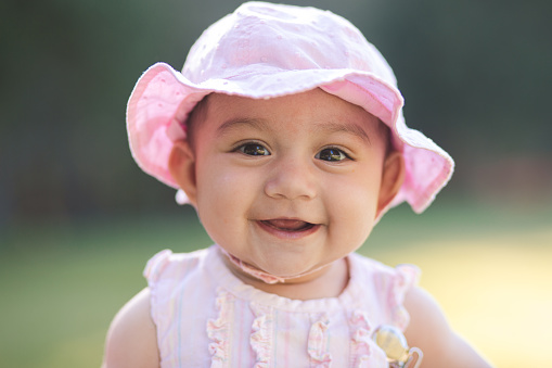 Portraits of a beautiful hispanic baby girl. She is wearing a cute pink outfit complete with a summer time pink hat. She is loving her day. She is smiling and so happy.