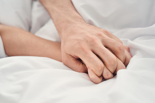 Close up of a Caucasian man and a woman with intertwined fingers making love in bed