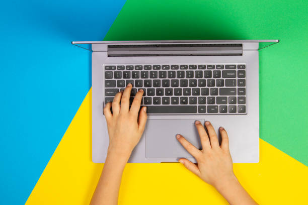 istock Kid hands typing on laptop computer keyboard on multicolored background, top view 1224514914
