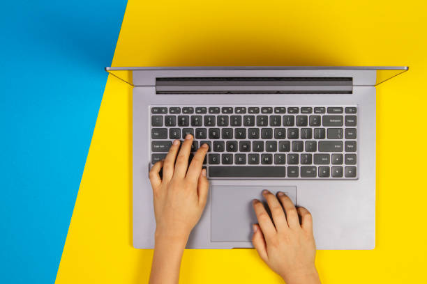 istock Kid hands typing on laptop computer keyboard, top view, yellow and blue background 1224515055
