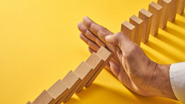 Gestão de risco de mão masculina, blocos de dominó caindo - foto de acervo
