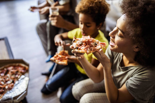 szczęśliwa czarna kobieta i jej rodzina o pizzę na lunch w domu. - pizza eating african descent lunch zdjęcia i obrazy z banku zdjęć