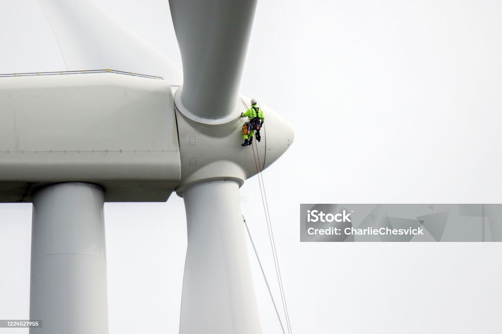 Rope access technicians rappelling down to working on blade of wind turbine and preparing rope protectors on the rope. Wind Turbine Stock Photo