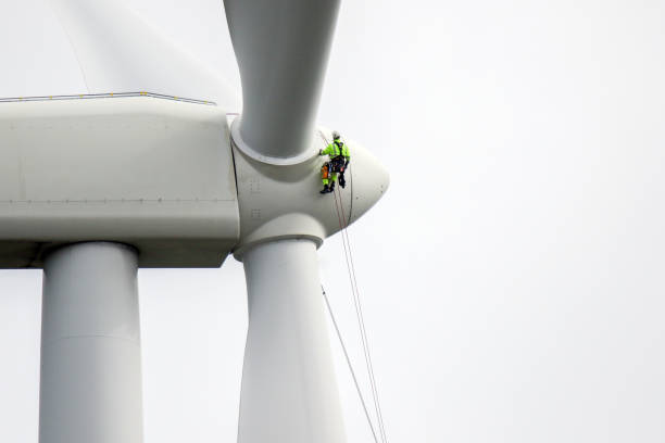 Rope access technicians rappelling down to working on blade of wind turbine and preparing rope protectors on the rope. stock photo