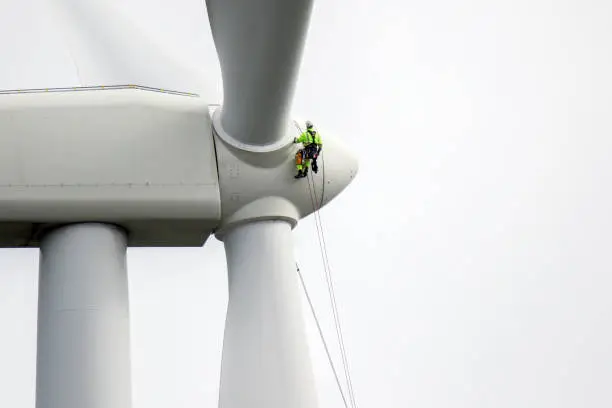 Rope access technicians rappelling down to working on blade of wind turbine and preparing rope protectors on the rope.