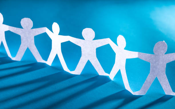 Human team of paper chain people. Team of paper chain people. Human chain with light and shadow. Blue tone background. line of people holding hands stock pictures, royalty-free photos & images