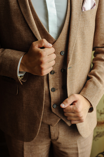 A man in a brown three-piece suit. Hands hold on to the sides of the jacket. Close-up