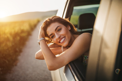 Happy young woman enjoying summer road trip through countryside
