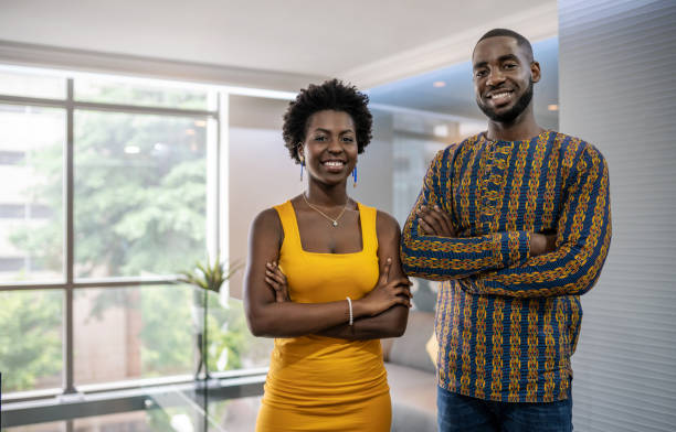 Two confident young African businesspeople standing in a modern Portrait of a two smiling young African businesspeople standing confidently with their arms crossed in a modern office west africa stock pictures, royalty-free photos & images