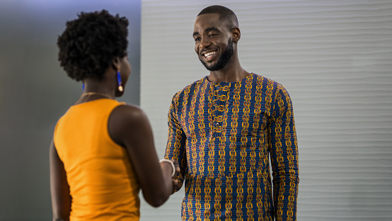 Two young African businesspeople smiling and shaking hands together while standing in a modern office