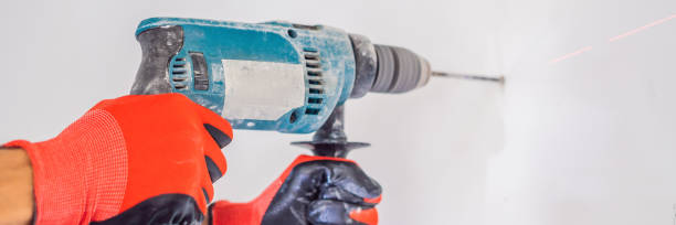 istock A man makes a hole in the wall with a drill BANNER, LONG FORMAT 1224531907