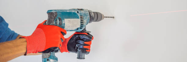 istock A man makes a hole in the wall with a drill BANNER, LONG FORMAT 1224531910