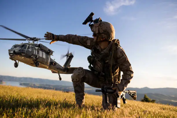 Military helicopter approaching behind the kneeling army soldier