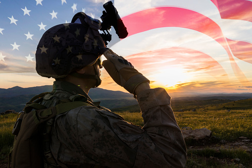 Silueta de un solider saludando contra la bandera de EE.UU. en el amanecer photo