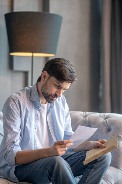 istock Serious man with a letter in hands sitting on couch. 1224537487