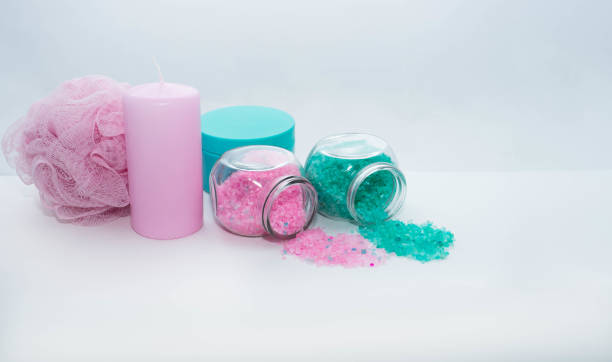 Two cans of bath salt of light pink and turquoise color, a turquoise jar of cream, a light pink candle and a sponge for a shower lie next to a white background. Body cosmetics and spa items. foto horizontal de cuidado personal, ducha y artículos de spa sobre el fondo blanco. esponja de ducha, vela y sal de baño en rosa claro y un tarro de crema y sal de baño turquesa. los objetos están cerca. los bancos están acostados de su lado. la sal