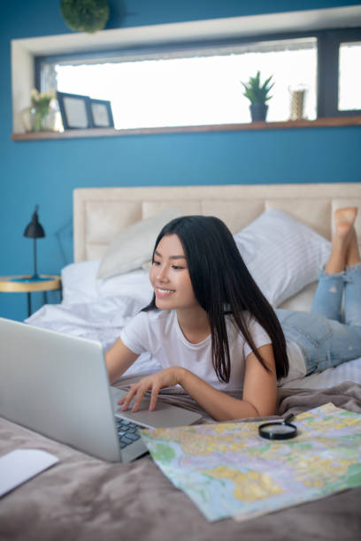 Young brunette lying on bed, typing something on laptop