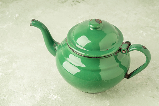closeup of an enameled retro teapot on green background