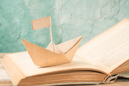paper boat on an old book on table. Hand crafted origami paper sailing boat on an opened book