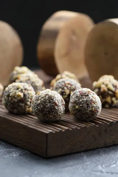 Healthy raw vegan sweets. Homemade energy balls with hazelnuts and wood slabs on dark oak board on black background closeup