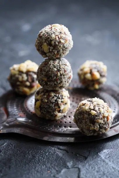 Healthy raw vegan sweets. Homemade energy balls with hazelnuts and wood slabs on dark oak board on black background copy space