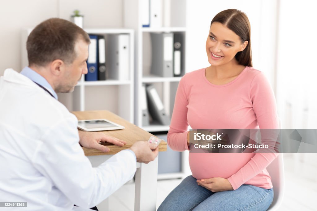 Médecin expérimenté mûr affichant des pillules au patient enceinte - Photo de Abdomen libre de droits Médecin expérimenté mûr affichant des pillules au patient enceinte - Photo de Abdomen libre de droits
