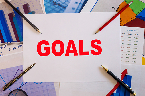 The word GOALS written on a white sheet of paper on the background of graphs next to pencils