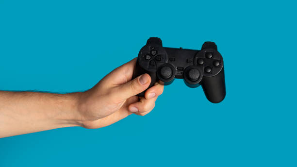 istock Stay home hobby. Millennial guy holding video game controller on blue background, closeup. Panorama 1224542973