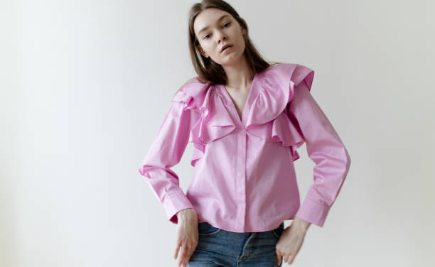 schöne junge frau mit nackten farbe make-up trägt rosa hemd und blaue jeans auf weißem hintergrund - puffed sleeve stock-fotos und bilder