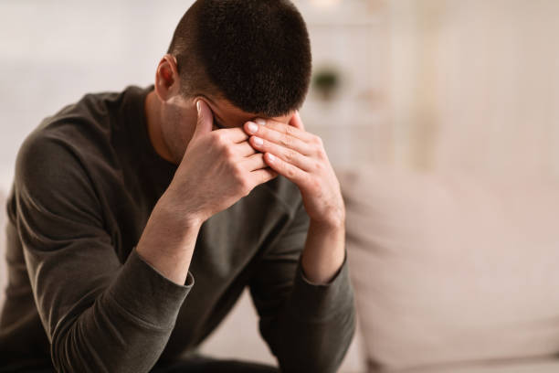 istock Ill man sitting on sofa with head on his hands 1224545215