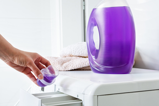 Woman hand pouring liquid detergent in the washing machine. Household.