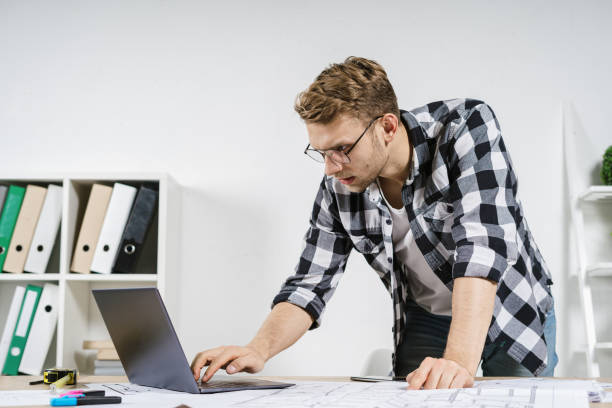 istock Young adult architect working with blueprints in workspace office 1224546974