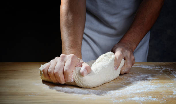 Hands kneading bread or pizza dough on a wooden pastry board.