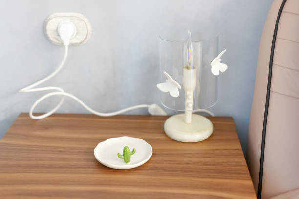 The lamp on the bedside table is plugged in. On the table is a saucer with a figure of a green cactus.