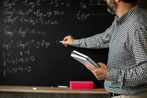 Male math professor writing mathematical formula on blackboard during online class