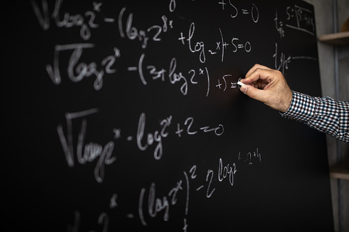 Male math professor writing mathematical formula on blackboard during online class, close-up