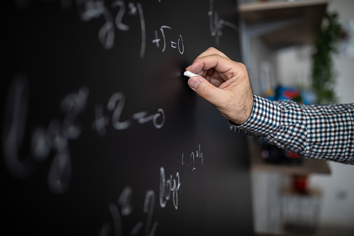 Male math professor writing mathematical formula on blackboard during online class, close-up