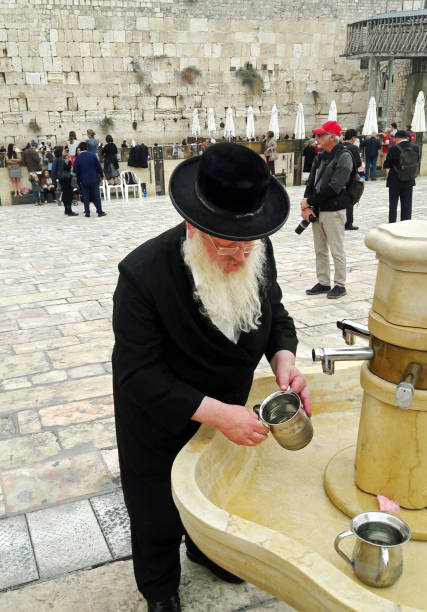 Woman wearing a straw hat and white shirt drinking water from a public fountain on a sunny day. Concept of hydration, summer, and outdoor activity.