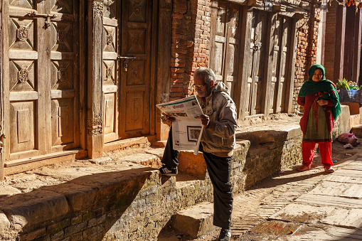 Dhulikhel, Nepal - November 15, 2016: Nepalese man reading a newspaper on the street.