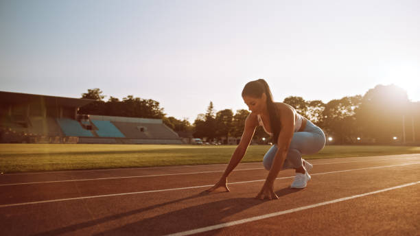 ライトブルーアスレチックトップとレギンスの美しいフィットネスウーマンは、屋外スタジアムでスプリントランを開始しています。彼女は暖かい夏の日に走っています。アスリートは彼女� - starting line competition running jogging ストックフォトと画像