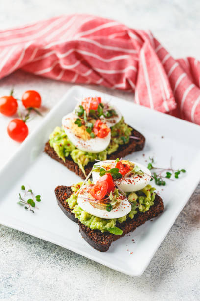 Toast with avocado and egg Healthy toast on rye bread with avocado, boiled eggs, spices, cherry tomatoes and microgreen on plate. Delicious appetizer, snack. egg cherry tomato rye stock pictures, royalty-free photos & images