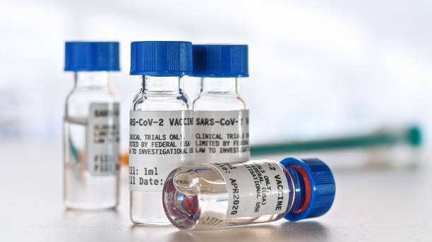 istock Coronavirus sars-CoV-2 vaccine concept, small vials with blue caps on white desk, blurred syringe background. (Sticker is own design with dummy data - not a real product) 1224566036