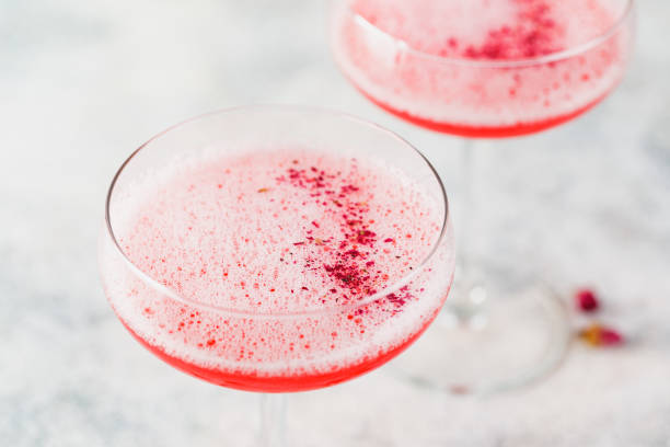 Pink Raspberry Cocktail in drink glass Pink alcoholic cocktail with lemonade, champagne or Martini in a champagne glass, with froth and decorated with dry rosebuds, cocktail like Daiquiri, Cosmopolitan, Pink Mimosa or Margarita Gin stock pictures, royalty-free photos & images