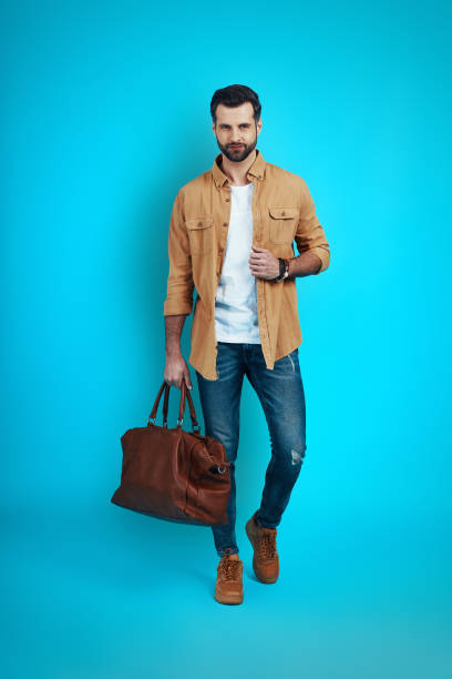 istock Full length of handsome young man smiling looking at camera while walking against blue background 1224567305