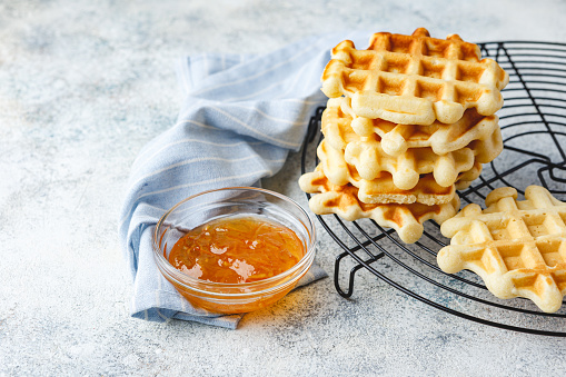 Traditional belgian homemade waffles with blueberry, honey and orange jam on metal grid on light background.
