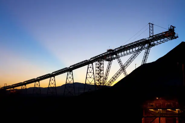 Sunrise behind silhouetted stockpile and conveyor belt in a copper mine at the Atacama Desert, Chile
