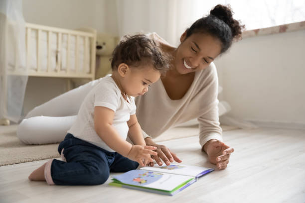 szczęśliwa afroamerykańska mama bawi się z małym dzieckiem - baby book toddler reading zdjęcia i obrazy z banku zdjęć
