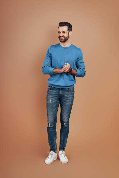 istock Full length of charming young man smiling and looking away while standing against brown background 1224568732